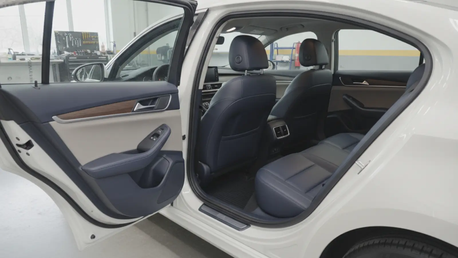 The clean interior of a car seen through an open rear door, parked in a bright garage workshop